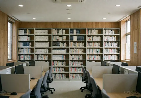 Bibliothèque technique équipée d'étagères métalliques remplies de livres, de chariots d'étude et de chaises ergonomiques, avec des murs en bois et une lumière naturelle.