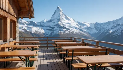 Terrasse en bois équipée de tables et de bancs offrant une vue panoramique sur des montagnes enneigées, refuge de montagne en hiver.