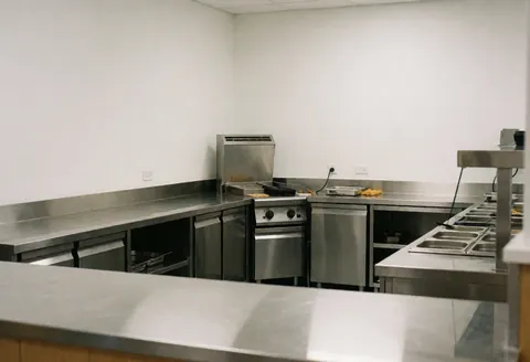 Cuisine professionnelle équipée d'une cuisinière industrielle, de tables en acier inoxydable et de murs blancs, adaptée à un centre de loisirs.