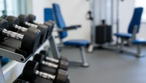 Arrière-plan de gymnase avec haltères et machines d'entraînement, idéal pour les textes sur la préparation physique et la récupération.