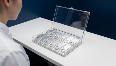Organisateur en acrylique contenant des bagues de nez et des boucles d'oreilles sur une table blanche avec des murs bleu foncé dans un studio de piercing professionnel.