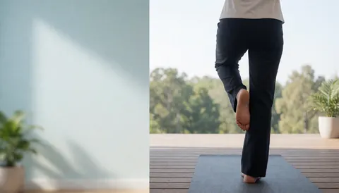 Une personne pratique le yoga en équilibre sur une natte posée sur une terrasse en bois, offrant une vue sur des arbres et la nature environnante.