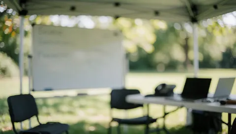 Scène professionnelle en extérieur avec tableau blanc, chaises et ordinateurs portables sur une table sous un auvent, idéal pour entraîneur de football.