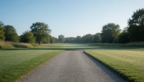 Chemin de gravier traversant un green tondé, avec des arbres en arrière-plan sous un ciel bleu clair, servant de fond neutre pour du texte.