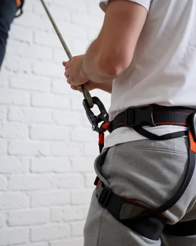 Vue rapprochée d'une personne utilisant une corde d'escalade et un harnais de sécurité sur un mur de briques blanches, illustrant l'équipement nécessaire pour des cours d'escalade en intérieur.