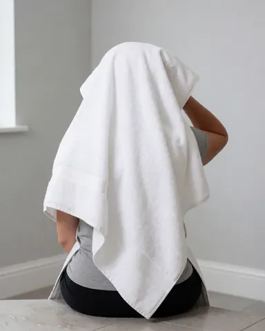 Une personne assise sur un sol carrelé avec des murs gris clair, séchant ses cheveux avec une serviette blanche, idéale pour une maison de vacances.