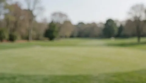 Arrière-plan flou d'un terrain de golf avec de l'herbe verte et des arbres au loin, idéal pour superposer du texte publicitaire.