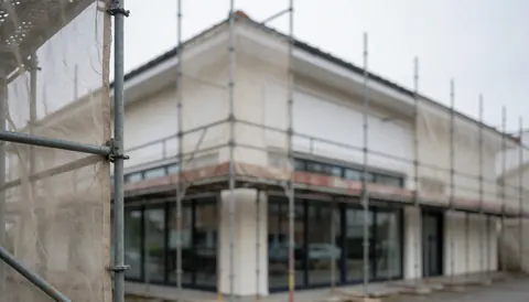 Façade d'un bâtiment commercial équipée d'échafaudages métalliques et d'un filet de protection, prête pour l'installation de fenêtres, dans un contexte de chantier professionnel.