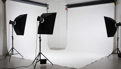 Studio photographique professionnel avec fond blanc et trois stands d'éclairage prêts pour des séances de portrait.