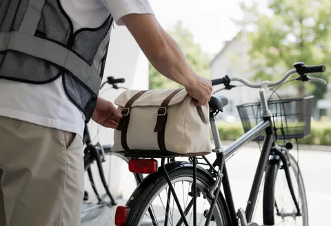 Un cycliste portant un gilet réfléchissant ajuste une sacoche en tissu sur le porte-bagages de son vélo dans un parking calme, se préparant pour une course en taxi vélo.