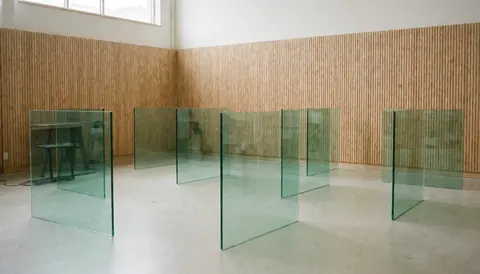 Panneaux de verre trempé debout dans un atelier avec murs en bois et sol en béton, éclairé par la lumière naturelle, idéal pour une entreprise de réparation de fenêtres.