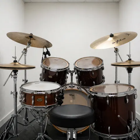 Ensemble complet de batterie acoustique avec cymbales et siège dans une salle de pratique pour académie de musique aux murs blancs et éclairage vif.