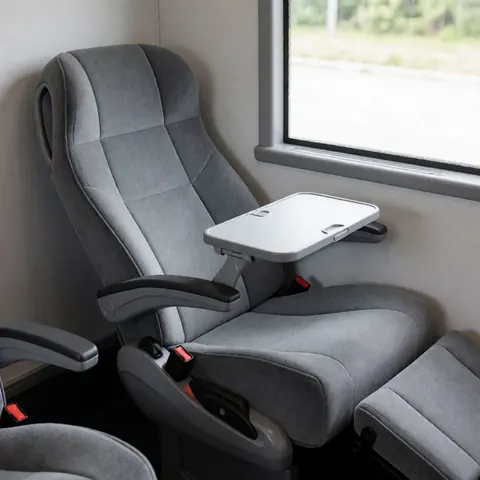 Siège de transport public moderne avec tablette déployée, parois grises et fenêtre laissant entrer la lumière naturelle pour un voyage confortable.