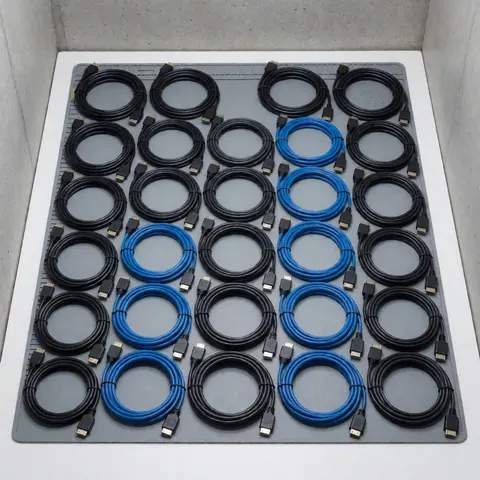 Câbles HDMI et LVDS rangés en rangées sur un tapis antistatique noir pour la réparation de téléviseurs, sur un fond en béton gris.