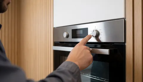 Technicien ajustant le cadran d'un four électrique moderne dans une cuisine avec murs en bois clair, idéal pour une entreprise de réparation de fours.