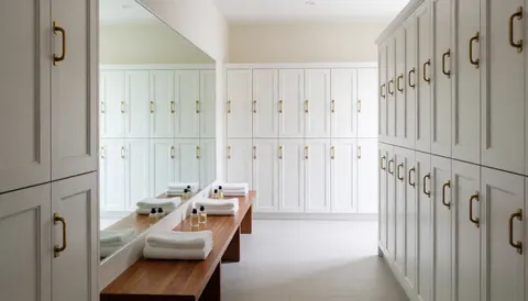 Vestiaire moderne avec casiers blancs, banc en bois et serviettes pliées, idéal pour un club de plage ou un spa.