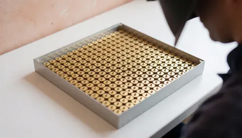Plateau avec des engrenages métalliques dans un atelier de réparation de montres, personne travaillant en arrière-plan, mur en plâtre terracotta, éclairage diffus.
