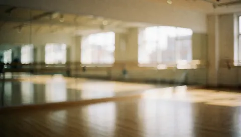 Intérieur d'un studio de danse moderne avec grands miroirs, sol en bois clair et barres de danse, offrant un fond neutre et lumineux idéal pour ajouter du texte.