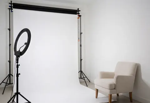 Studio photographique minimaliste au fond blanc, éclairage par anneau lumineux et chaise beige, idéal pour des portraits professionnels.