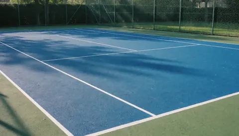 Cour de tennis fraîchement peinte en bleu vif avec lignes blanches nettes, entourée d'une clôture en maille chaînée, idéale pour illustrer des services d'installation.