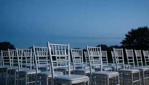 Scène de location de mobilier pour événements en plein air, rangées de chaises Chiavari métalliques sous un ciel bleu, idéale pour mariages ou galas formels.