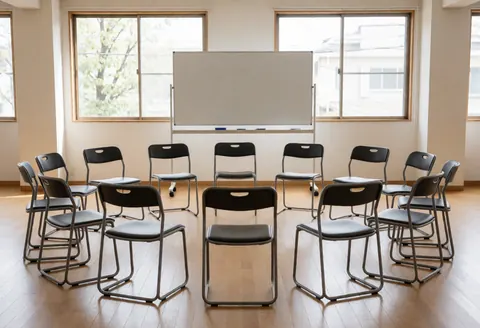 Salle de réunion avec chaises en cercle, tableau blanc et grandes fenêtres, idéale pour les ateliers créatifs et les sessions de groupe.