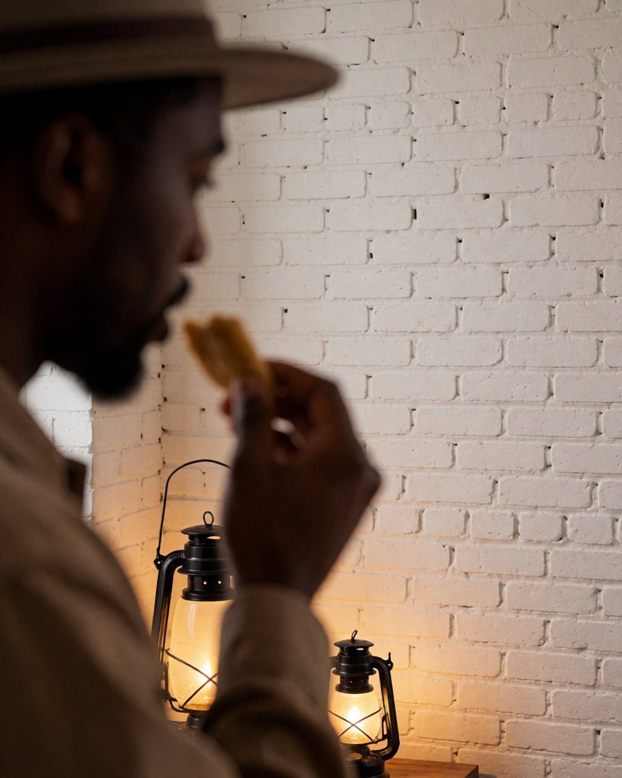 Un homme profite d'un repas traditionnel dans un festival nocturne, éclairé par des lanternes et devant un mur de briques blanches.