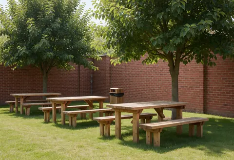 Espace pique-nique avec tables et bancs en bois sous des arbres, pelouse entretenue et mur de briques rouges, idéal pour un parc écologique.