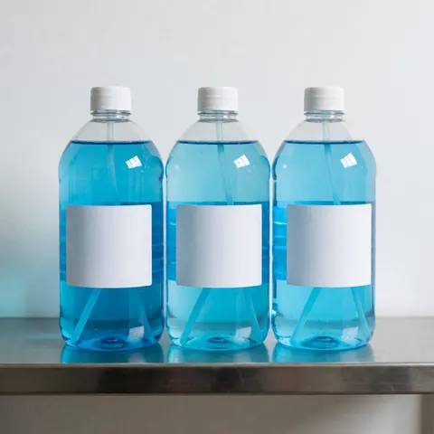 Trois bouteilles vides de désinfectant bleu avec étiquettes blanches posées sur une étagère en métal, adaptées à un usage commercial ou industriel.