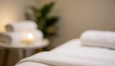 Lit de massage avec serviettes blanches, bougies allumées et plante verte dans un environnement chaleureux et relaxant pour spa.
