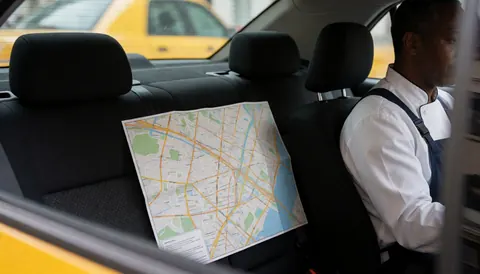 Vue intérieure d'un taxi montrant une carte urbaine posée sur le siège arrière, illustrant un service de transport en cours.