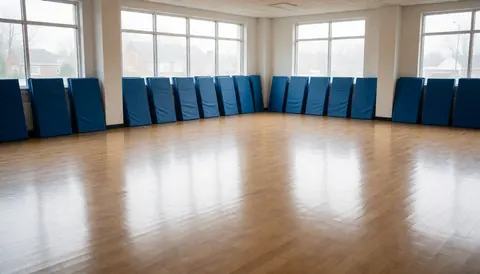 Dojo de karate vide avec des tapis bleus empilés contre les murs et un sol en bois poli, idéal pour une page d'accueil de site web.
