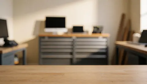 Arrière-plan d'atelier de réparation de meubles avec table en bois, armoire à outils et ordinateurs, éclairage chaleureux et rangé.