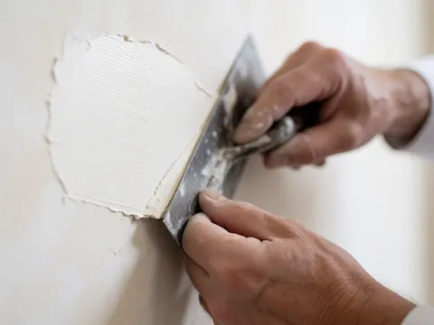 Gros plan d'une main tenant une truelle en train d'appliquer du plâtre sur une surface murale pour un fini professionnel.