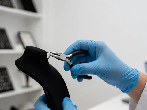 Une main portant un gant bleu ajuste un anneau de capture métallique sur un support noir dans un studio de tatouage avec des étagères d'accessoires en arrière-plan