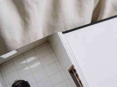 Gros plan montrant les coutures précises et la page brillante d'un livre photo à couverture rigide sur un fond de tissu doux et de carreaux blancs.