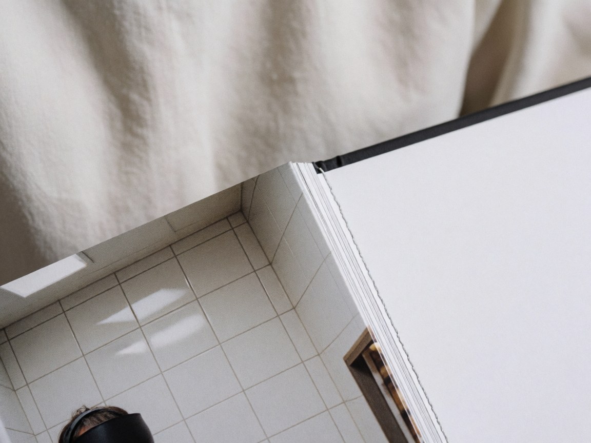 Gros plan montrant les coutures précises et la page brillante d'un livre photo à couverture rigide sur un fond de tissu doux et de carreaux blancs.
