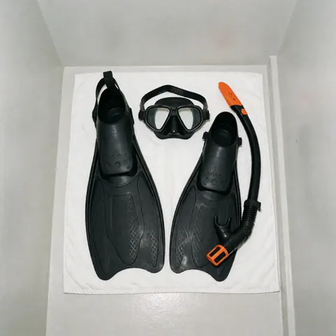 Masque de plongée, palmes noires et tuba orange posés sur une serviette blanche, équipement pour entraîneur de natation.