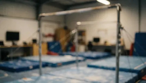 Arrière-plan flou d'un gymnase avec des barres d'équilibre et des tapis bleus, idéal pour du texte sur l'enseignement de la gymnastique.