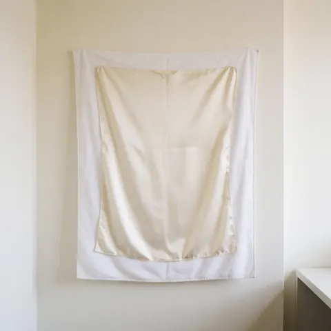 Serviette blanche sèche avec tissu en soie blanche posé dessus, sur un mur de couleur chaude, éclairage naturel, scène minimaliste et propre pour une laverie.
