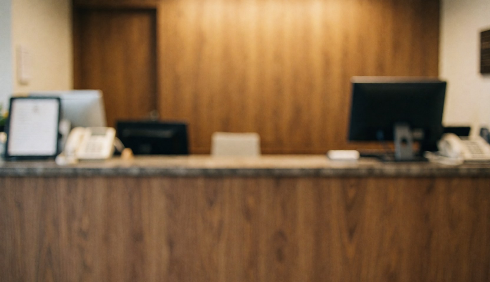 Réception de boutique d'horlogerie avec comptoir en bois, ordinateurs et téléphone, éclairage chaleureux et fond flou pour texte.