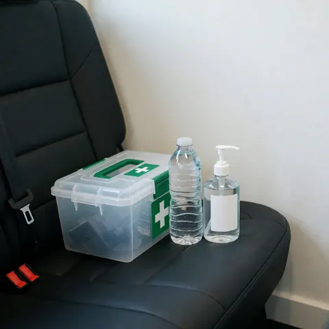 Kit de premiers secours, bouteille d'eau et désinfectant posés sur un siège de voiture noir devant un mur blanc pour un service de transport