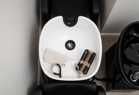 Station de lavage de cheveux propre et ordonnée dans un salon de beauté, avec serviette, brosses et chaise noire sur fond de murs gris chauds.