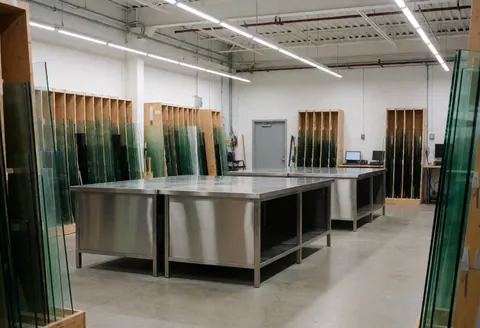 Atelier de vitrage équipé de tables en acier inoxydable, de racks de stockage pour verre et d'un sol en béton, idéal pour les installateurs de vitrage.