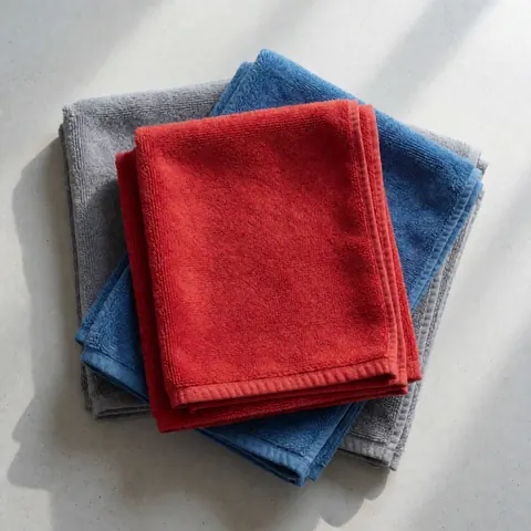 Serviettes en microfibre rouges, bleues et grises disposées sur un sol en béton pour le lavage des véhicules.