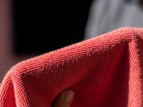 Chiffon en microfibre rouge pour le lavage de véhicules, détail de la texture et de la main tenant le tissu, fond flou noir et gris.