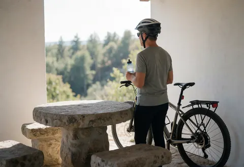 Un cycliste équipé d'un casque se repose près d'une table en pierre dans un belvédère avec une vue sur une forêt, idéal pour un business lié au cyclisme.