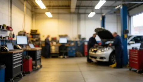 Deux mécaniciens examinent un véhicule avec le capot ouvert dans un atelier de réparation, entourés d'outils et d'un éclairage industriel sur un fond flou.