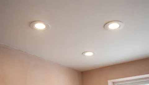 Plafond blanc avec trois spots LED encastrés allumés, murs en enduit terracotta, éclairage chaleureux et propre, idéal pour électricien résidentiel.