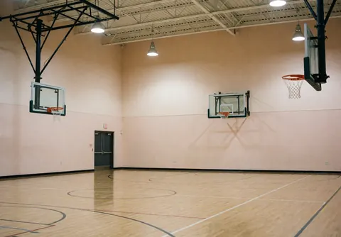 Gymnase de basket-ball vide avec sol en bois poli, murs beige et paniers prêts à jouer, idéal pour les installateurs de courts de tennis.